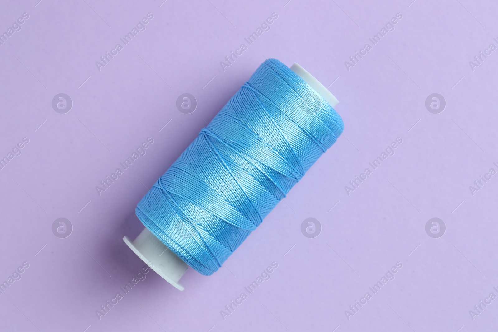 Photo of Spool of light blue sewing thread on lilac background, top view