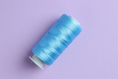 Photo of Spool of light blue sewing thread on lilac background, top view