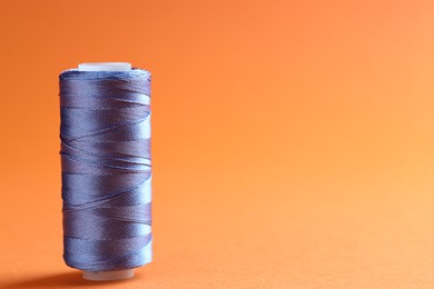 Photo of Spool of blue sewing thread on orange background, space for text