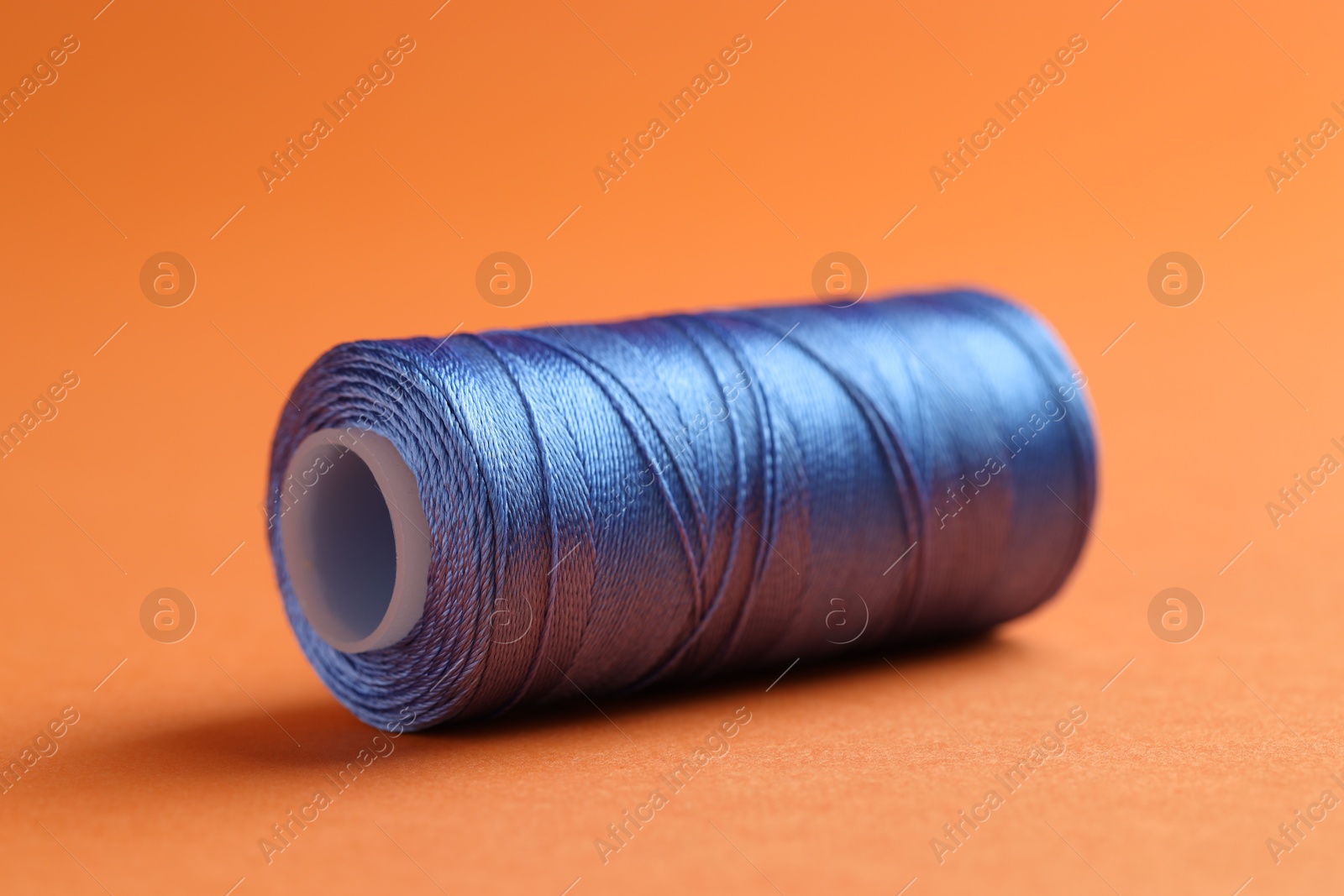 Photo of Spool of blue sewing thread on orange background, closeup