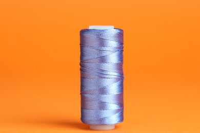 Photo of Spool of blue sewing thread on orange background