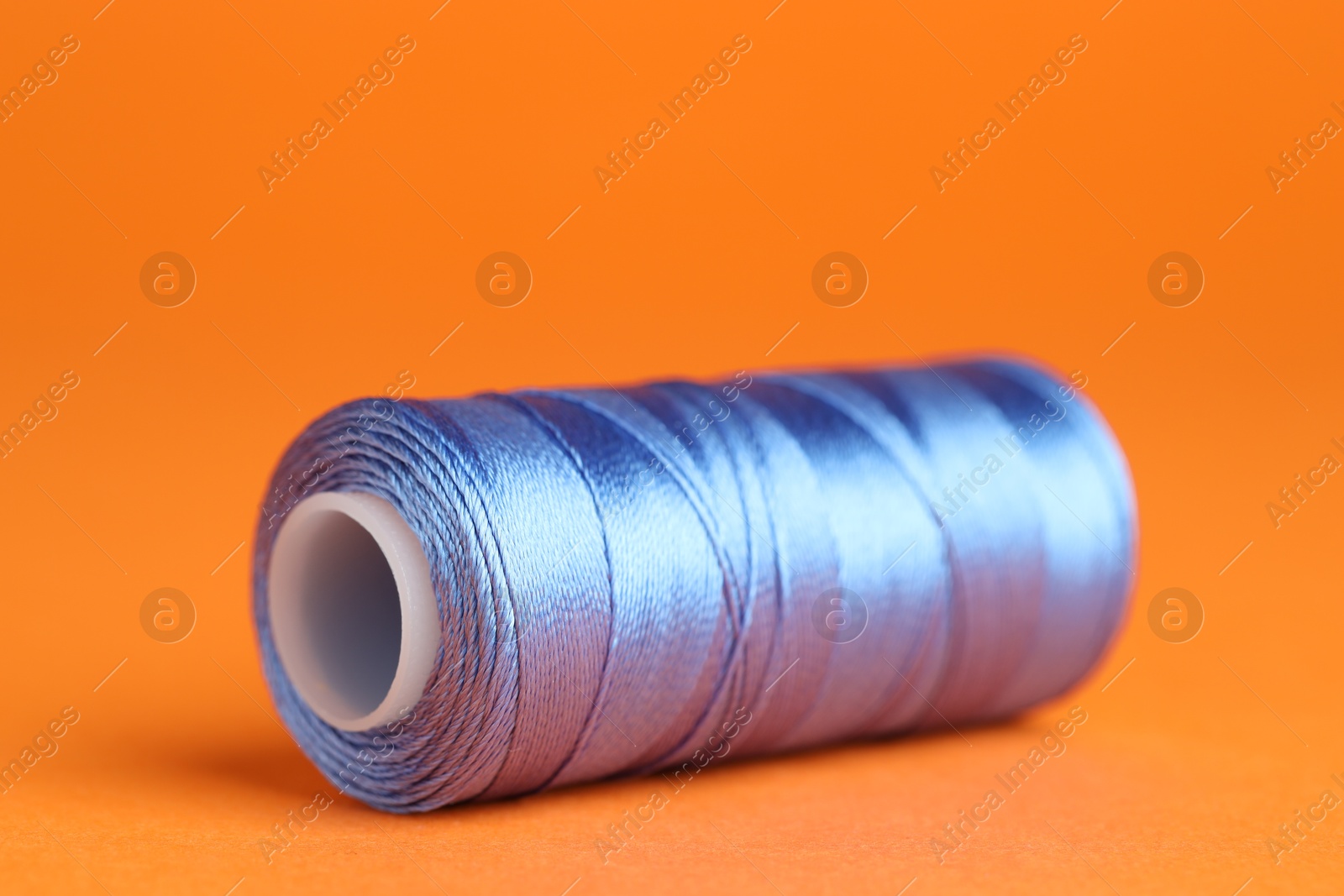 Photo of Spool of blue sewing thread on orange background, closeup