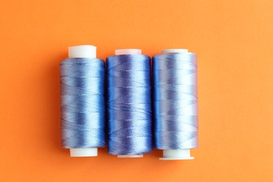 Photo of Spools of colorful sewing threads on orange background, flat lay