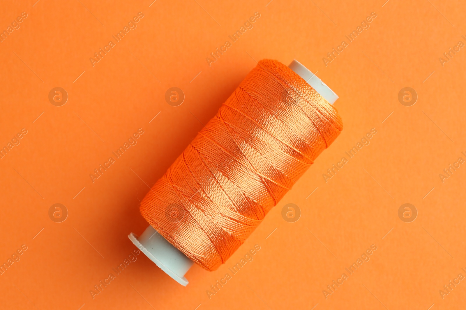 Photo of Spool of bright sewing thread on orange background, top view