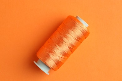 Photo of Spool of bright sewing thread on orange background, top view