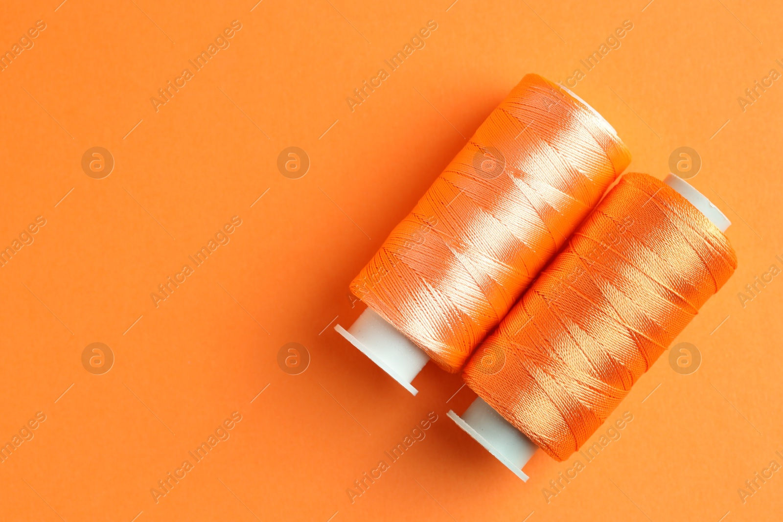 Photo of Spools of bright sewing threads on orange background, top view. Space for text