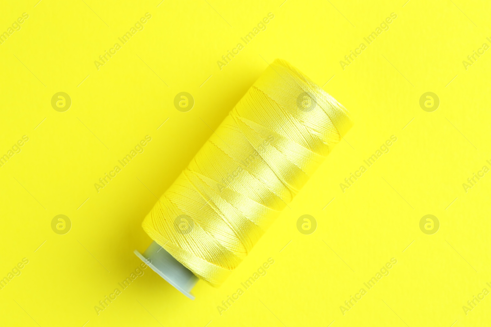 Photo of Spool of bright sewing thread on yellow background, top view