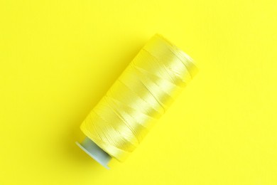 Photo of Spool of bright sewing thread on yellow background, top view