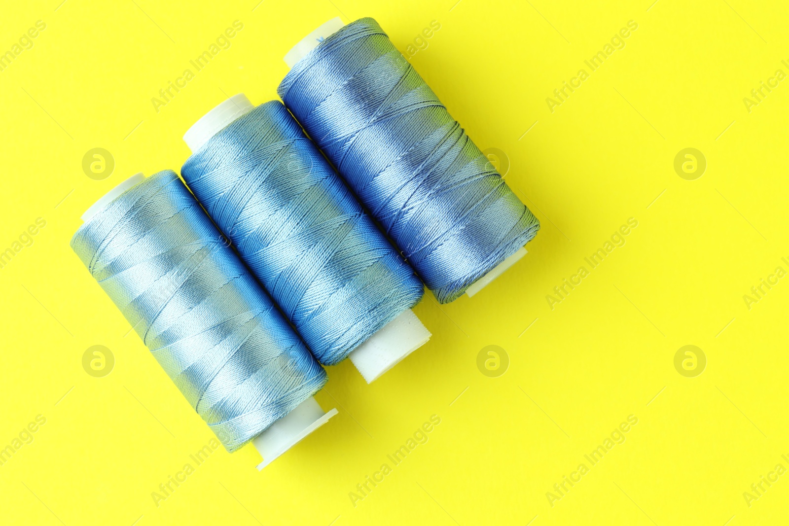 Photo of Spools of colorful sewing threads on yellow background, flat lay. Space for text