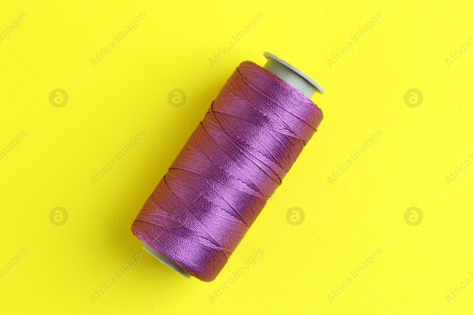 Photo of Spool of purple sewing thread on yellow background, top view