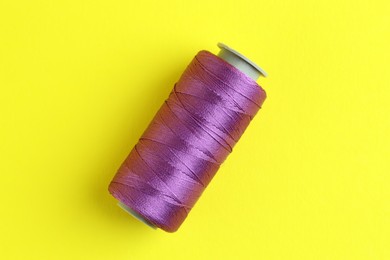 Photo of Spool of purple sewing thread on yellow background, top view