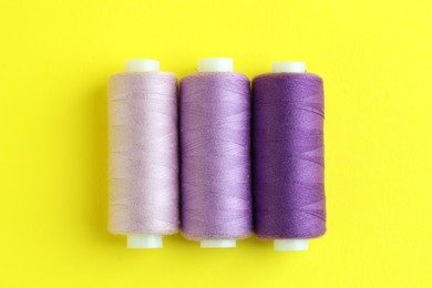 Photo of Spools of colorful sewing threads on yellow background, flat lay