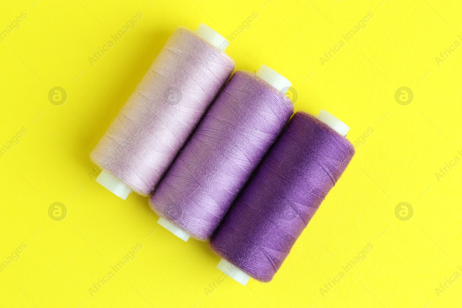 Photo of Spools of colorful sewing threads on yellow background, flat lay