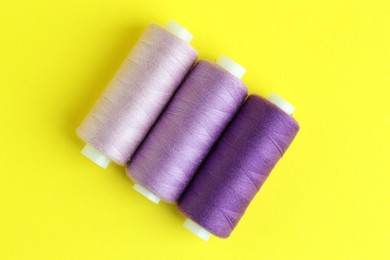 Photo of Spools of colorful sewing threads on yellow background, flat lay