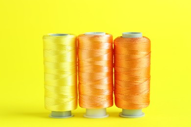 Photo of Spools of colorful sewing threads on yellow background