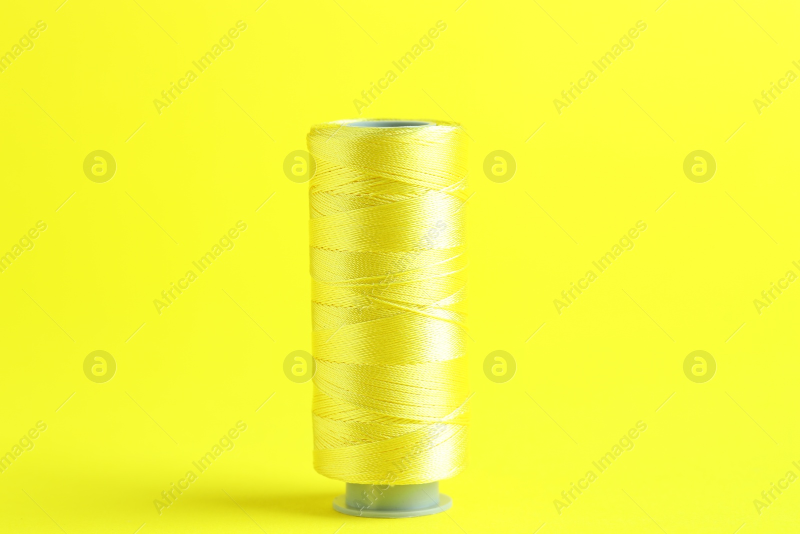 Photo of Spool of sewing thread on yellow background