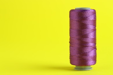 Photo of Spool of purple sewing thread on yellow background, space for text