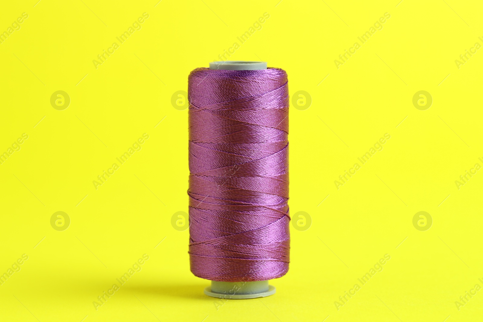 Photo of Spool of purple sewing thread on yellow background