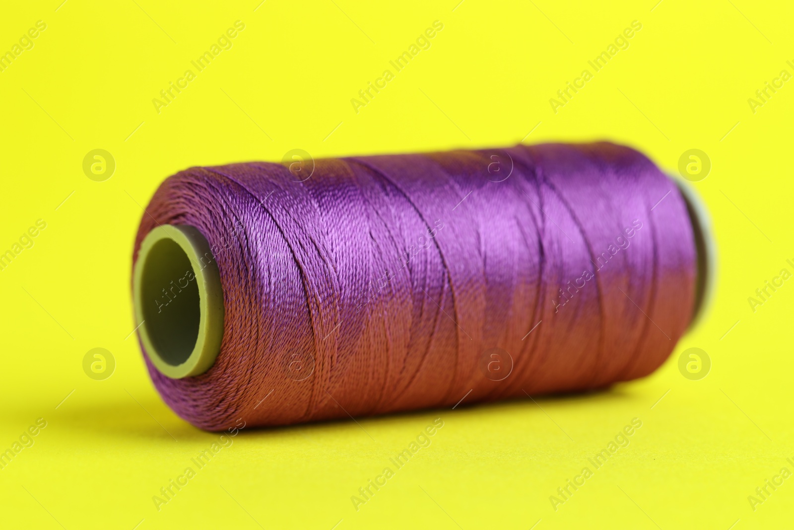 Photo of Spool of purple sewing thread on yellow background, closeup