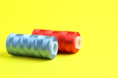 Photo of Spools of colorful sewing threads on yellow background, closeup. Space for text