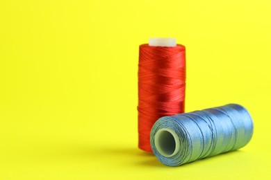 Photo of Spools of colorful sewing threads on yellow background, closeup. Space for text