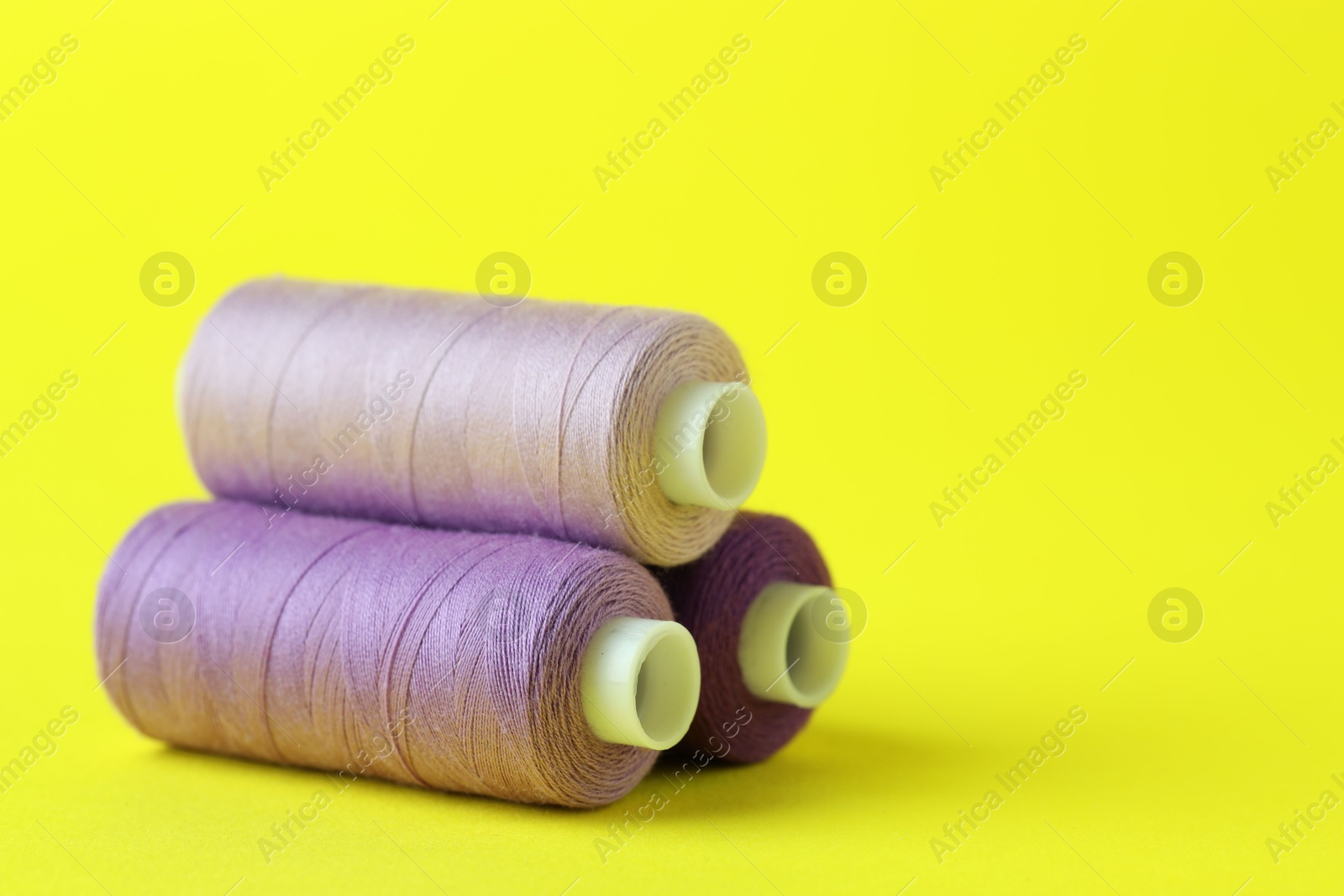 Photo of Spools of colorful sewing threads on yellow background, closeup. Space for text