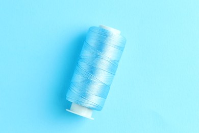 Photo of Spool of sewing thread on light blue background, top view