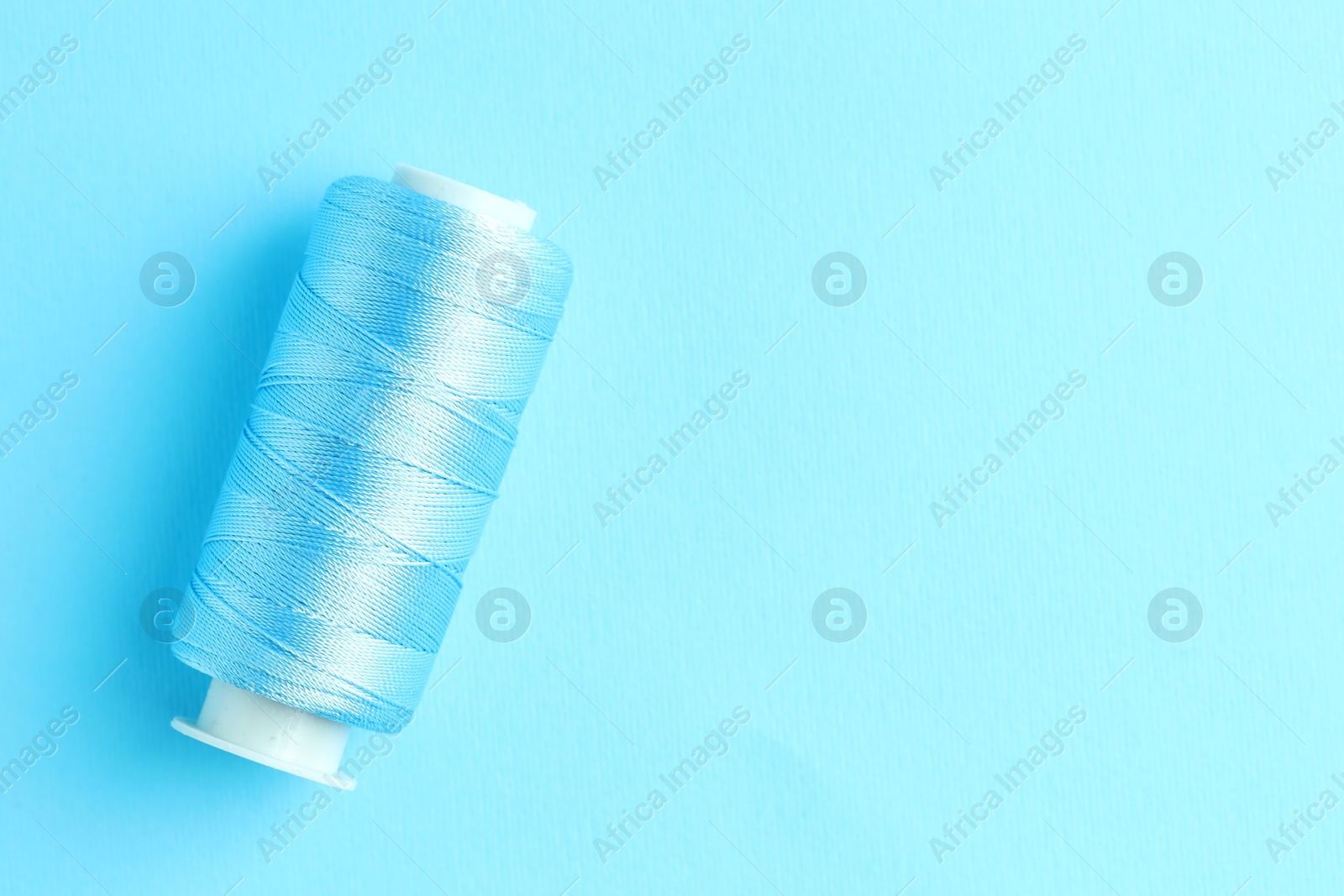 Photo of Spool of sewing thread on light blue background, top view. Space for text