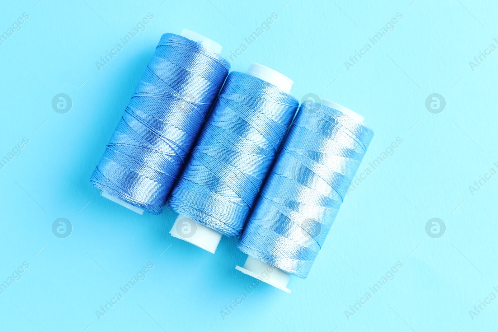 Photo of Spools of colorful sewing threads on light blue background, flat lay