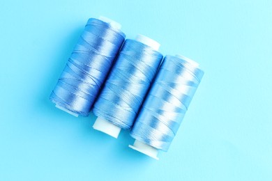 Photo of Spools of colorful sewing threads on light blue background, flat lay