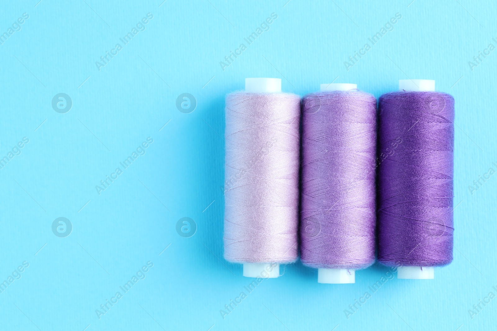 Photo of Spools of colorful sewing threads on light blue background, flat lay. Space for text