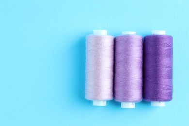 Photo of Spools of colorful sewing threads on light blue background, flat lay. Space for text