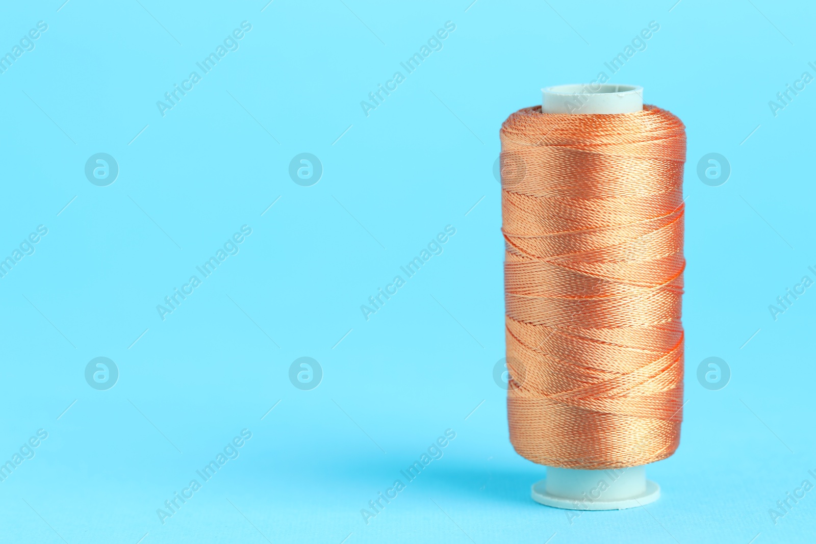 Photo of Spool of orange sewing thread on light blue background, space for text