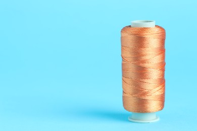 Photo of Spool of orange sewing thread on light blue background, space for text