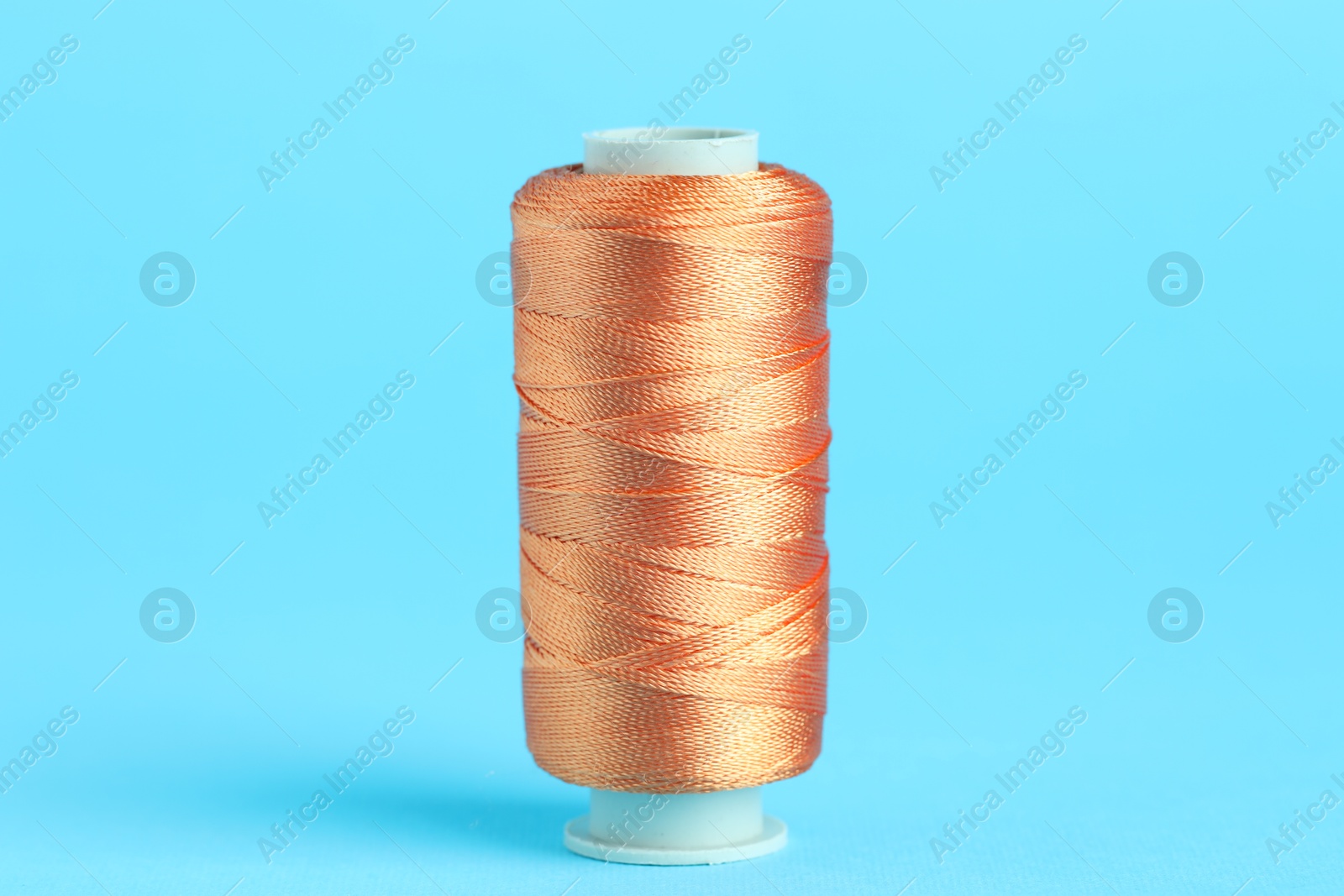 Photo of Spool of orange sewing thread on light blue background