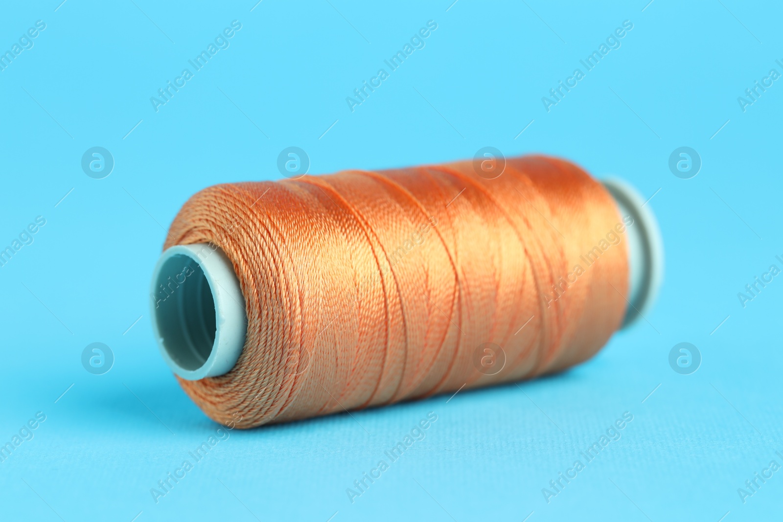 Photo of Spool of orange sewing thread on light blue background, closeup