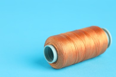 Photo of Spool of orange sewing thread on light blue background, closeup. Space for text