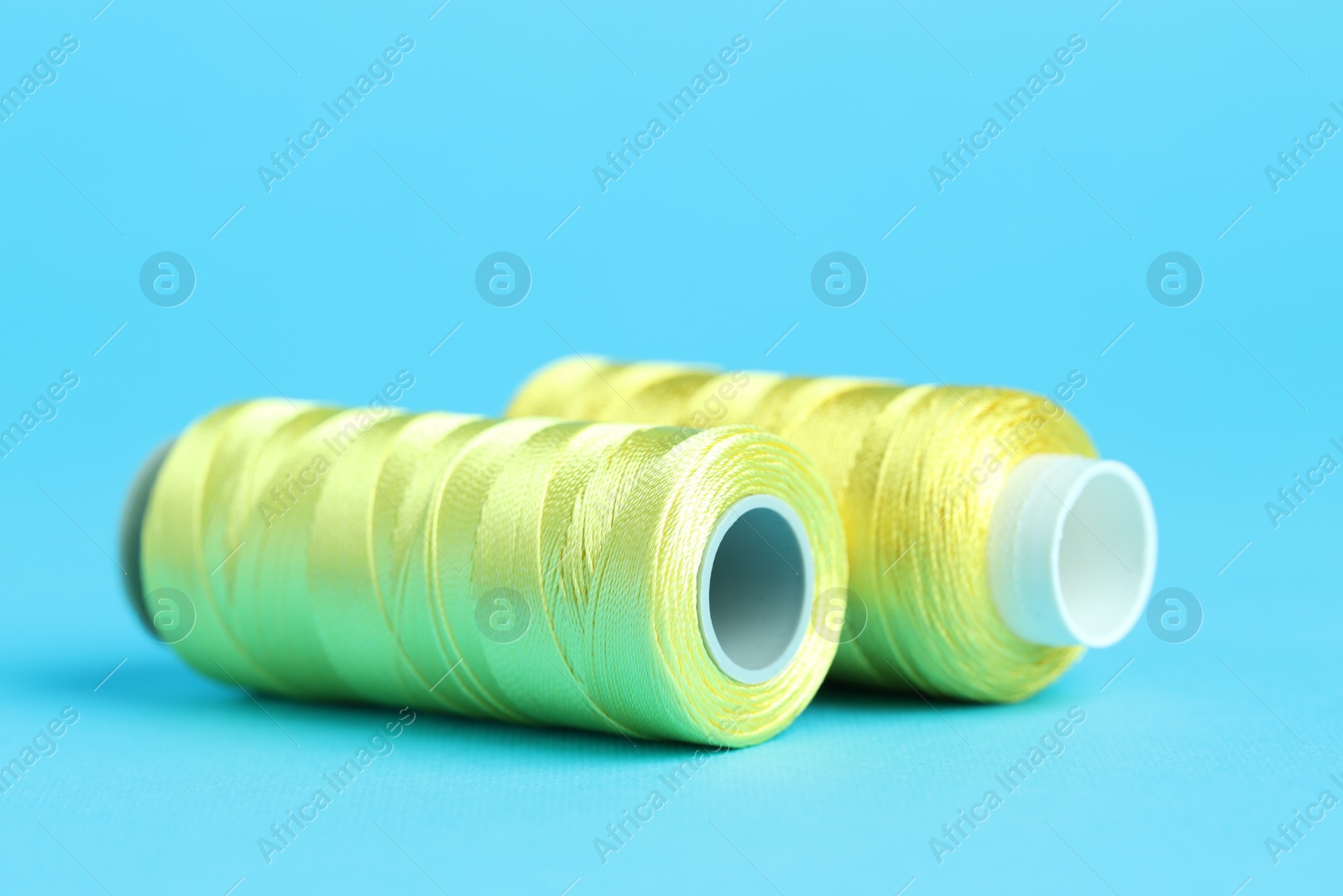 Photo of Spools of yellow sewing threads on light blue background, closeup