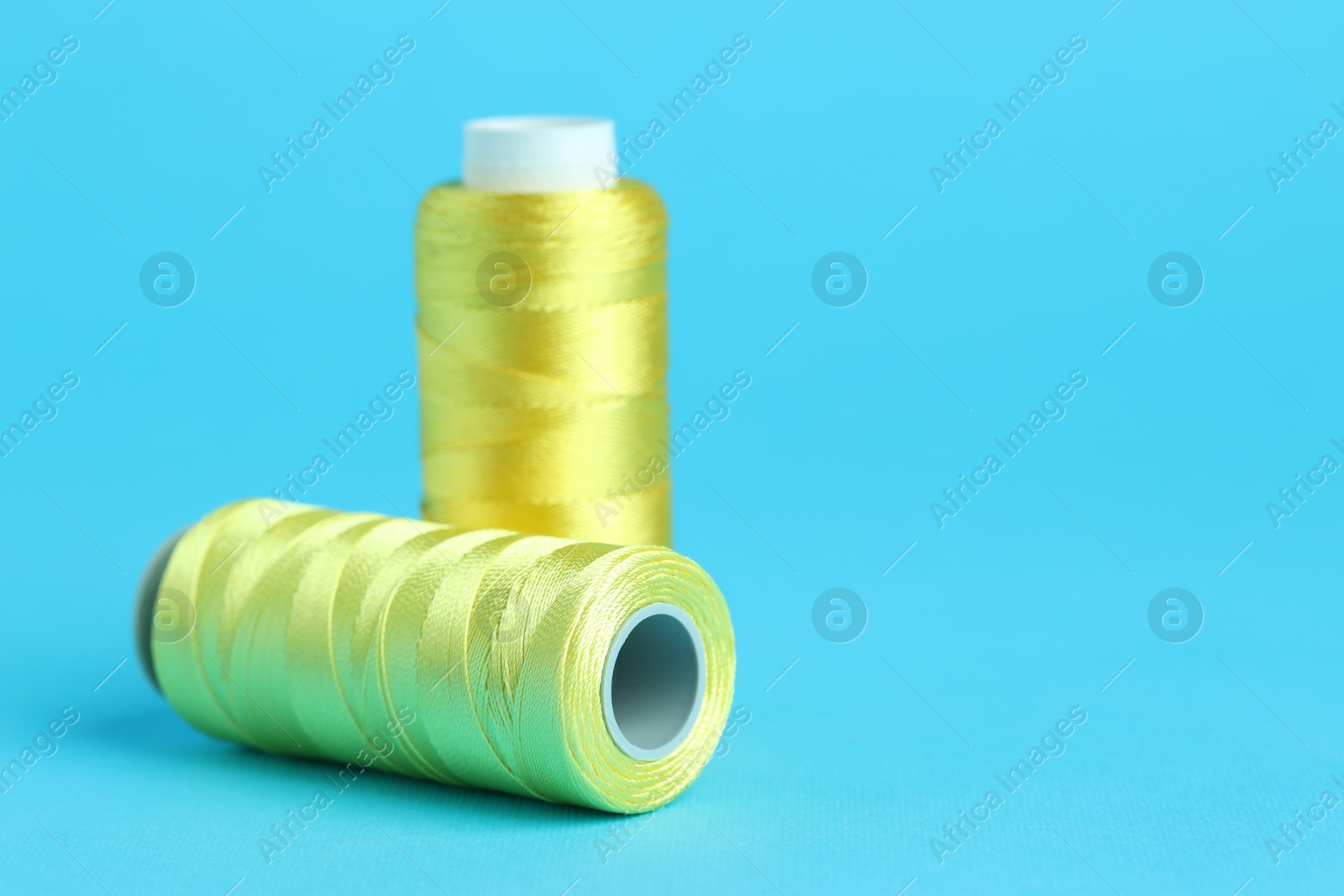 Photo of Spools of yellow sewing threads on light blue background, closeup. Space for text