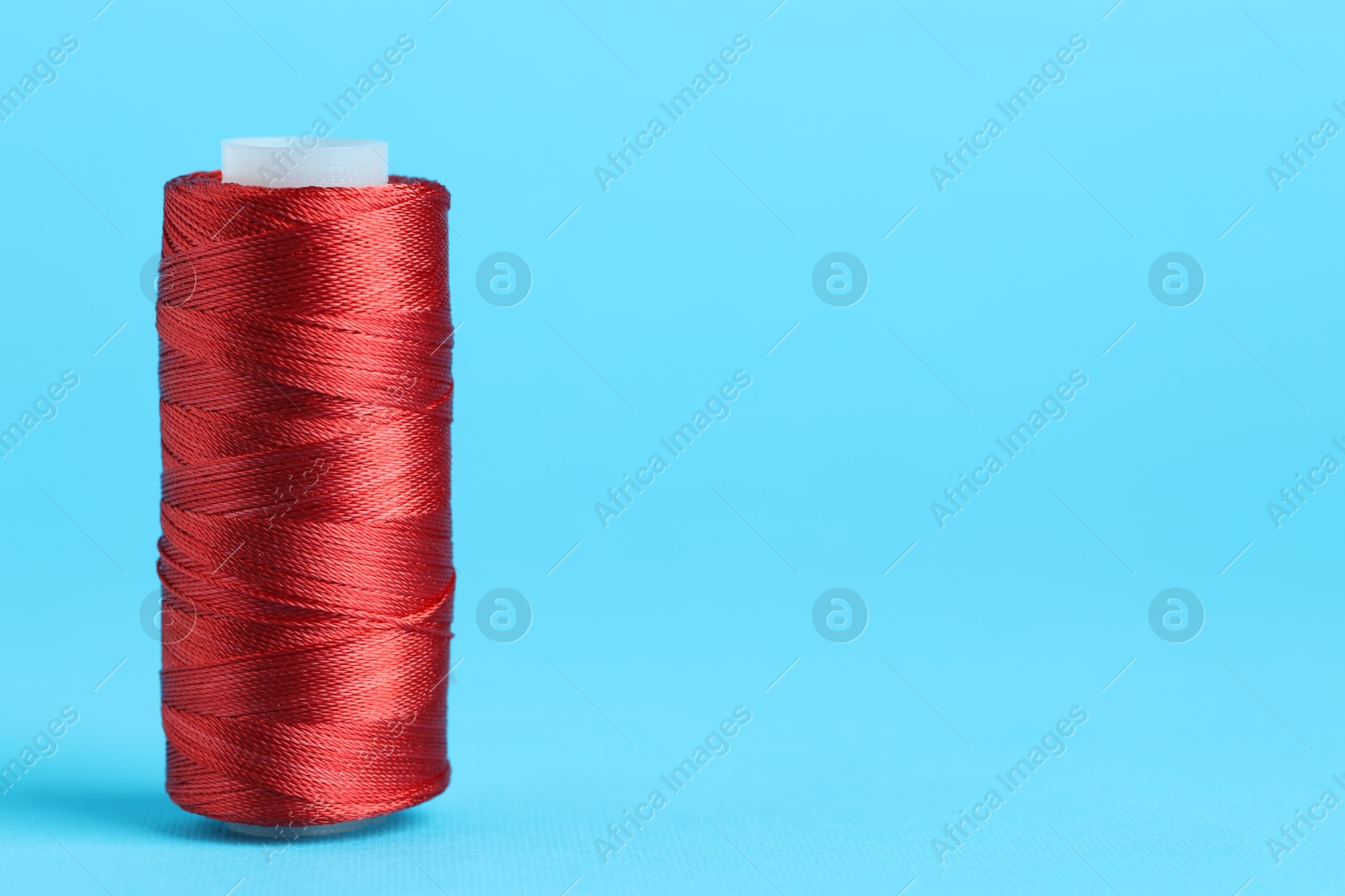 Photo of Spool of red sewing thread on light blue background, space for text