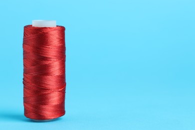 Photo of Spool of red sewing thread on light blue background, space for text