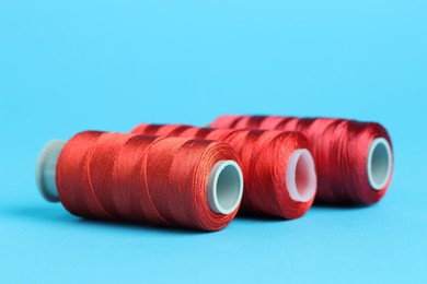 Photo of Spools of red sewing threads on light blue background, closeup