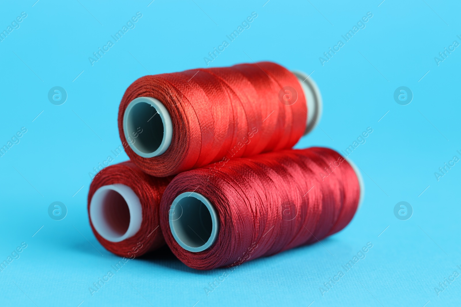 Photo of Spools of red sewing threads on light blue background, closeup