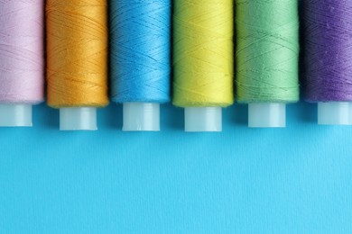 Photo of Spools of colorful sewing threads on light blue background, flat lay. Space for text