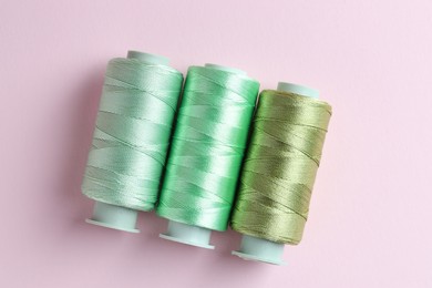 Photo of Spools of colorful sewing threads on pink background, flat lay