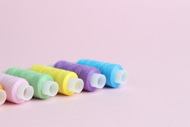 Photo of Spools of colorful sewing threads on pink background, closeup. Space for text