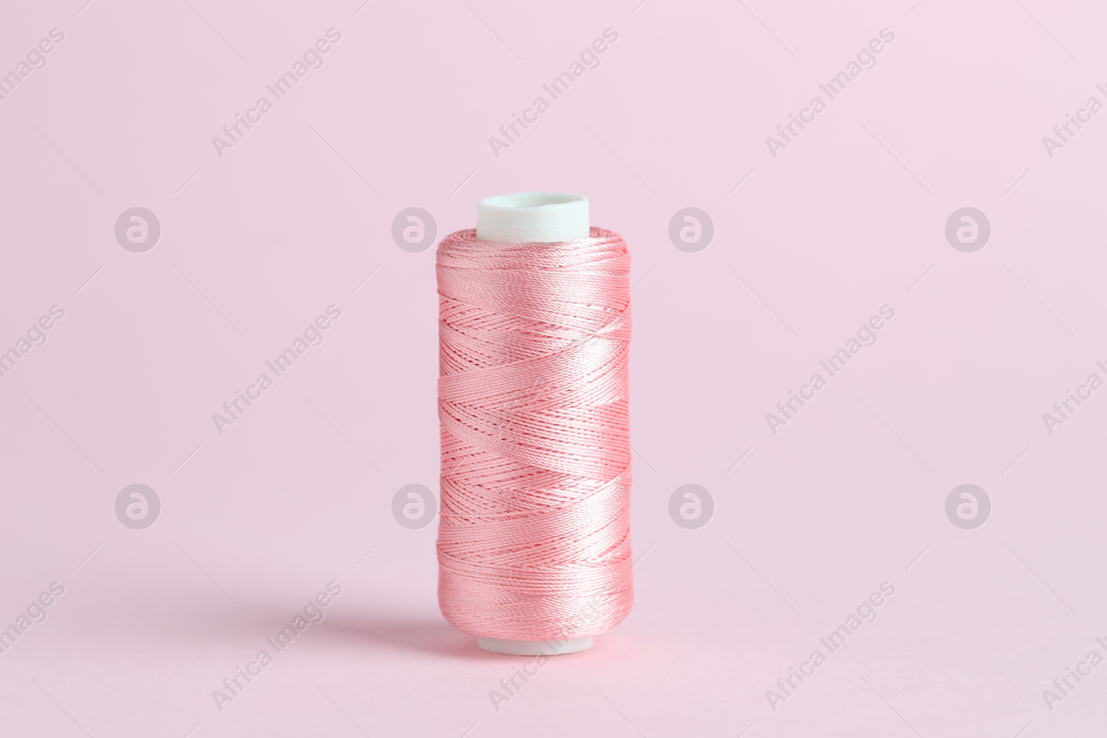 Photo of Spool of sewing thread on pink background