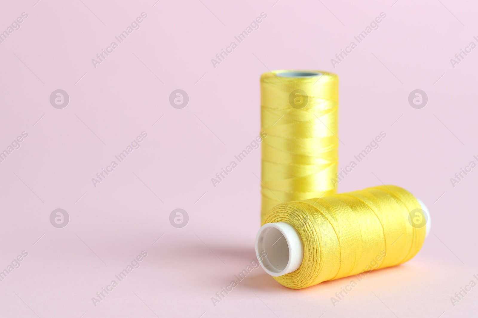 Photo of Spools of yellow sewing threads on pink background, closeup. Space for text