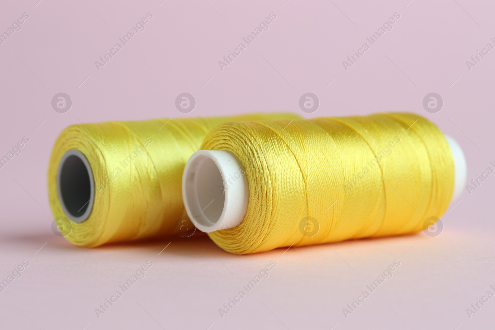 Photo of Spools of yellow sewing threads on pink background, closeup