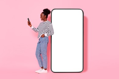 Image of Happy woman with smartphone leaning on big mobile phone with blank screen on pink background